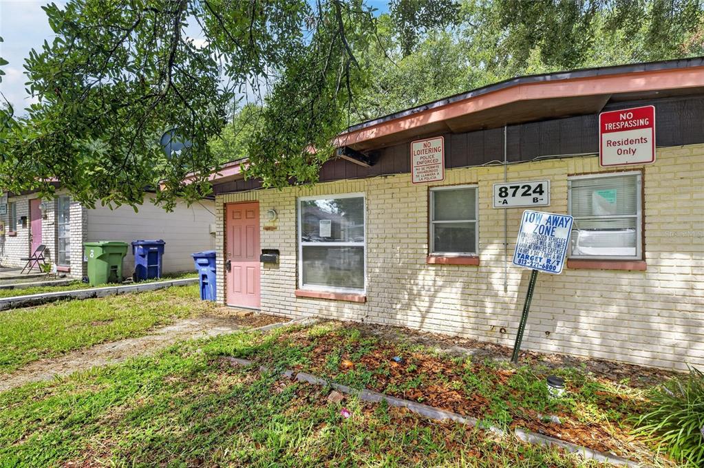 A single-story brick building with a pink door, multiple signs, and outdoor trash bins — 8723 & 8724 N 48TH STREET, TAMPA, FL