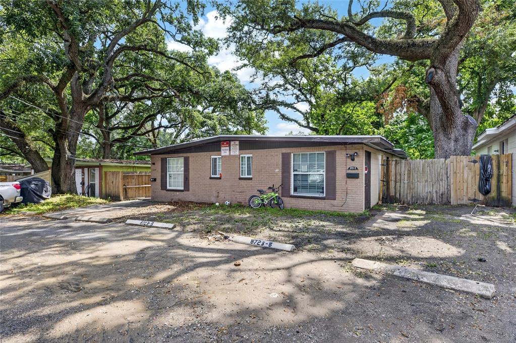 A single-story brick duplex with a dirt parking area and large oak trees — 8723 & 8724 N 48TH STREET, TAMPA, FL