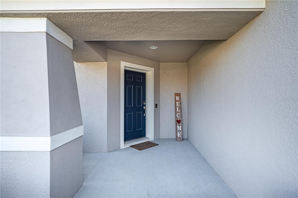 A covered concrete porch features a dark blue front door and a vertical welcome sign — 8256 CAMPBELL CROSSING CIRCLE, LAKELAND, FL