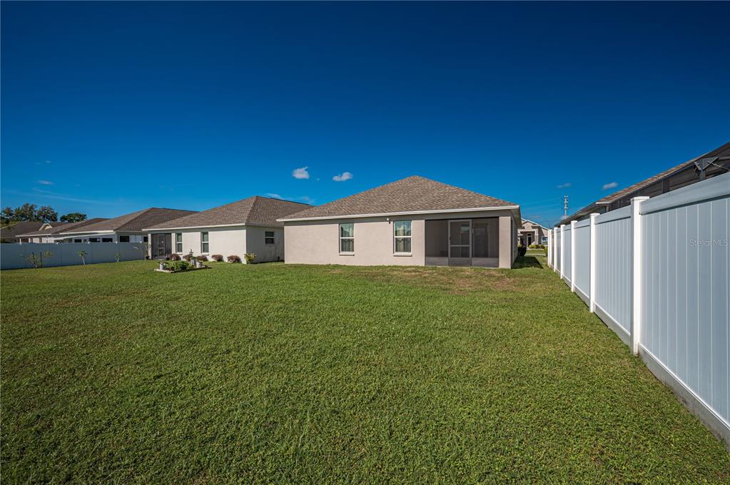 The backyard of a house features a lawn, a screened-in patio, and white vinyl fencing — 8256 CAMPBELL CROSSING CIRCLE, LAKELAND, FL