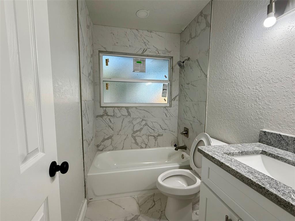 A bathroom features a marble-tiled tub surround, a white toilet, and a granite-topped vanity — 1030 SE 18TH TERRACE, GAINESVILLE, FL