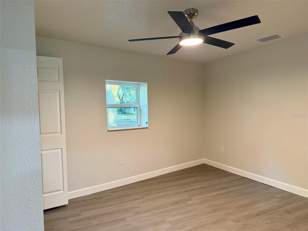 A bedroom features light gray walls, wood-look flooring, a ceiling fan, and a white door — 1030 SE 18TH TERRACE, GAINESVILLE, FL