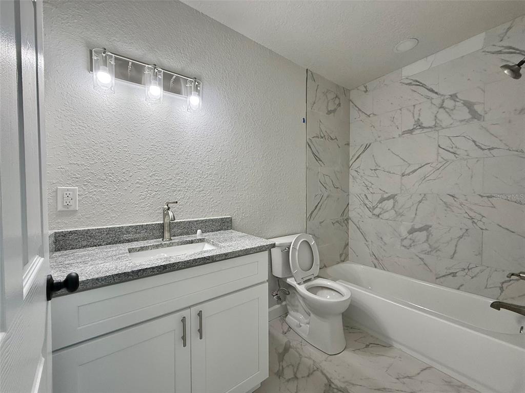 A bathroom features a white vanity with a granite countertop, a toilet, and a tiled tub — 1030 SE 18TH TERRACE, GAINESVILLE, FL
