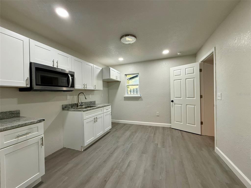 A kitchen features white cabinets, granite countertops, a microwave, and light-colored wood-look flooring — 1030 SE 18TH TERRACE, GAINESVILLE, FL