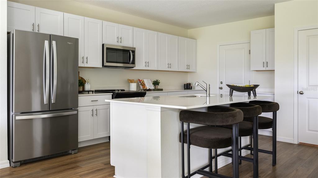 A modern kitchen features white cabinets, stainless steel appliances, a quartz island, and dark stools — 33623 NOBLE CREEK PLACE, DADE CITY, FL