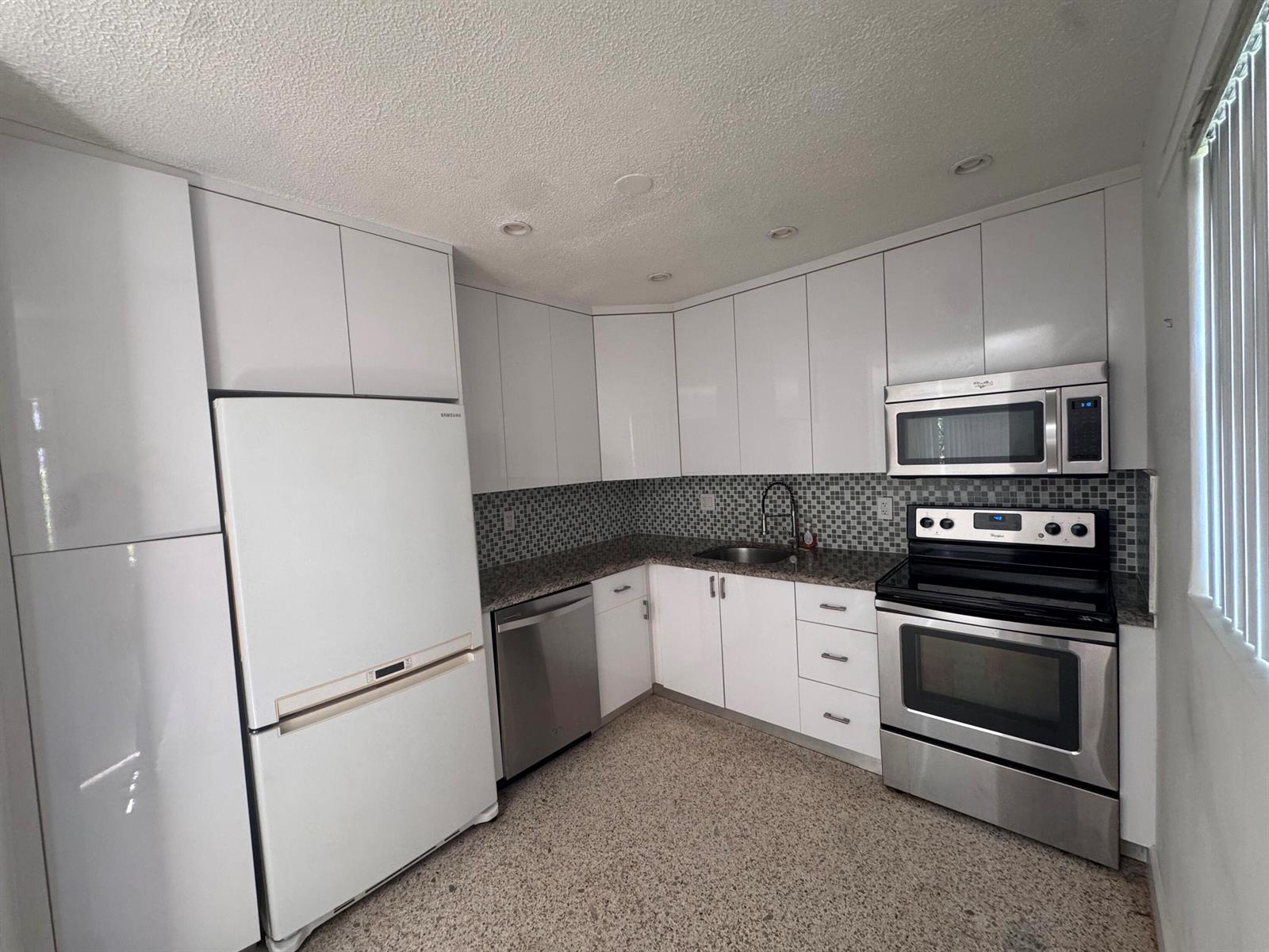 A kitchen features white flat-panel cabinets, stainless steel appliances, and a speckled stone countertop — 570 NE 64th Street Unit 4, Miami FL 33138, MIAMI, FL