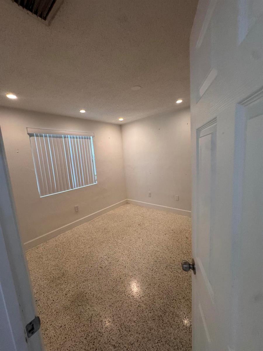 An empty room with white walls, recessed lighting, and speckled terrazzo flooring — 570 NE 64th Street Unit 4, Miami FL 33138, MIAMI, FL