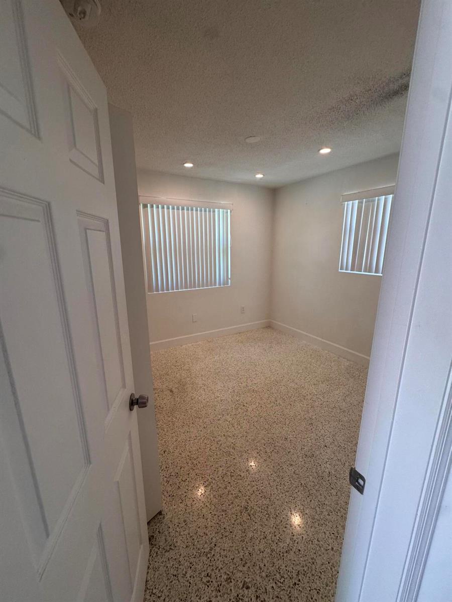 An empty bedroom features white walls, recessed lighting, vertical blinds, and speckled terrazzo flooring — 570 NE 64th Street Unit 4, Miami FL 33138, MIAMI, FL