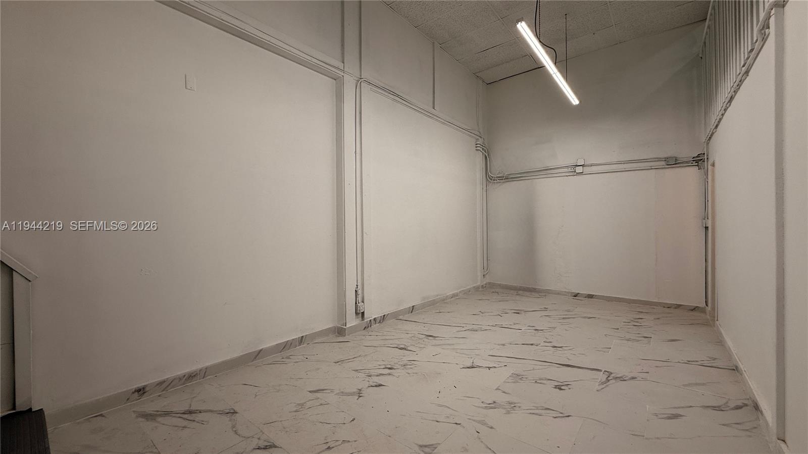 An empty room features white walls, marble-patterned tile flooring, and a single hanging light fixture — 500 NE 25th St # 5, Pompano Beach FL 33064, POMPANO BEACH, FL