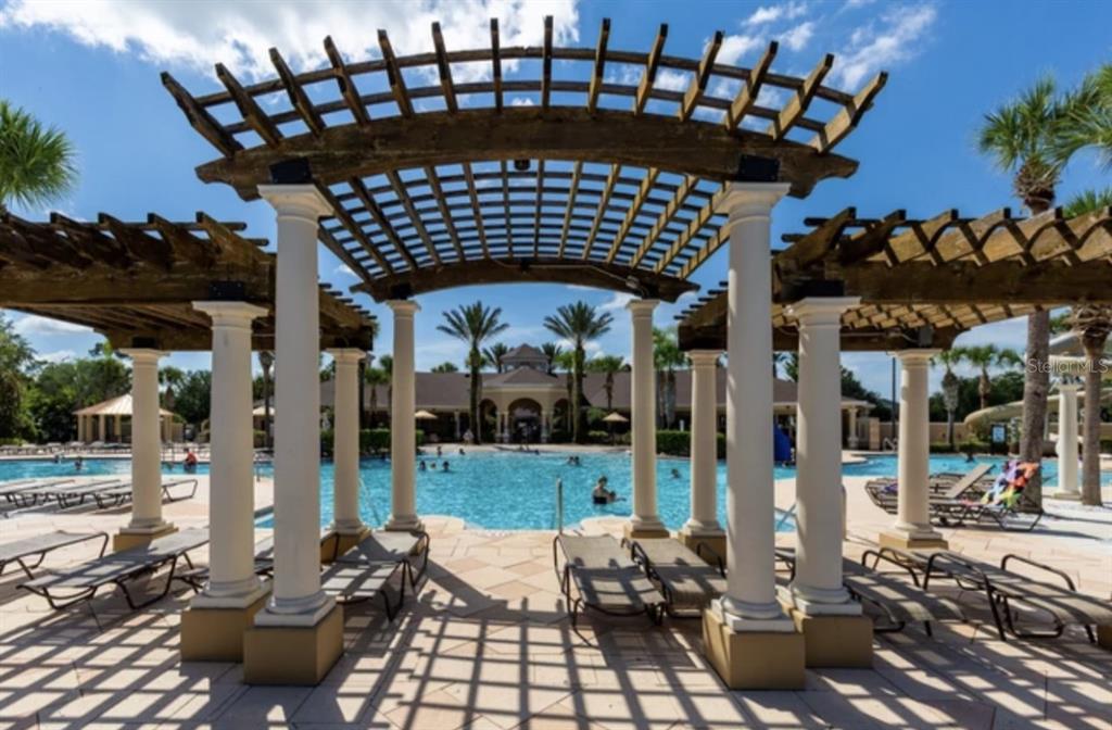 A wooden pergola with white columns overlooks a swimming pool with lounge chairs on a patio — 2534 MANESHAW LANE, KISSIMMEE, FL