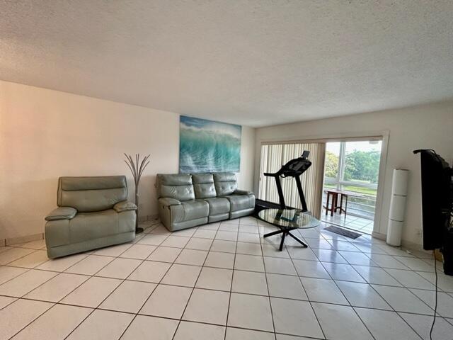 A living room features light-colored tile flooring, a gray sofa and armchair, and a treadmill — 3601 Inverrary Drive # 306, Lauderhill FL 33319, LAUDERHILL, FL