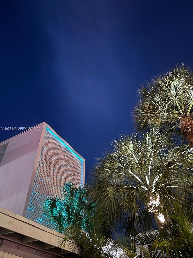 A low-angle view of a modern building exterior with illuminated brickwork and palm trees — 2101 Normandy Dr # 310, Miami Beach FL 33141, MIAMI BEACH, FL