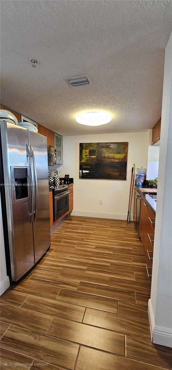 A galley kitchen features stainless steel appliances, wood-look tile flooring, and wood cabinetry — 1800 N Bayshore Dr # 3808, Miami FL 33132, MIAMI, FL