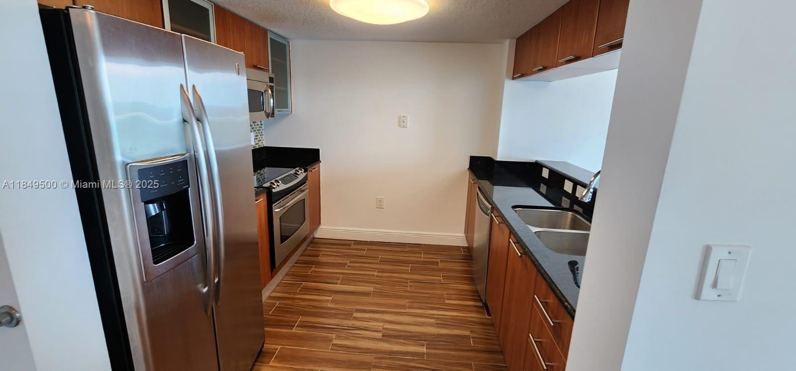 A galley-style kitchen features stainless steel appliances, wood-toned cabinetry, and dark countertops — 1800 N Bayshore Dr # 3808, Miami FL 33132, MIAMI, FL