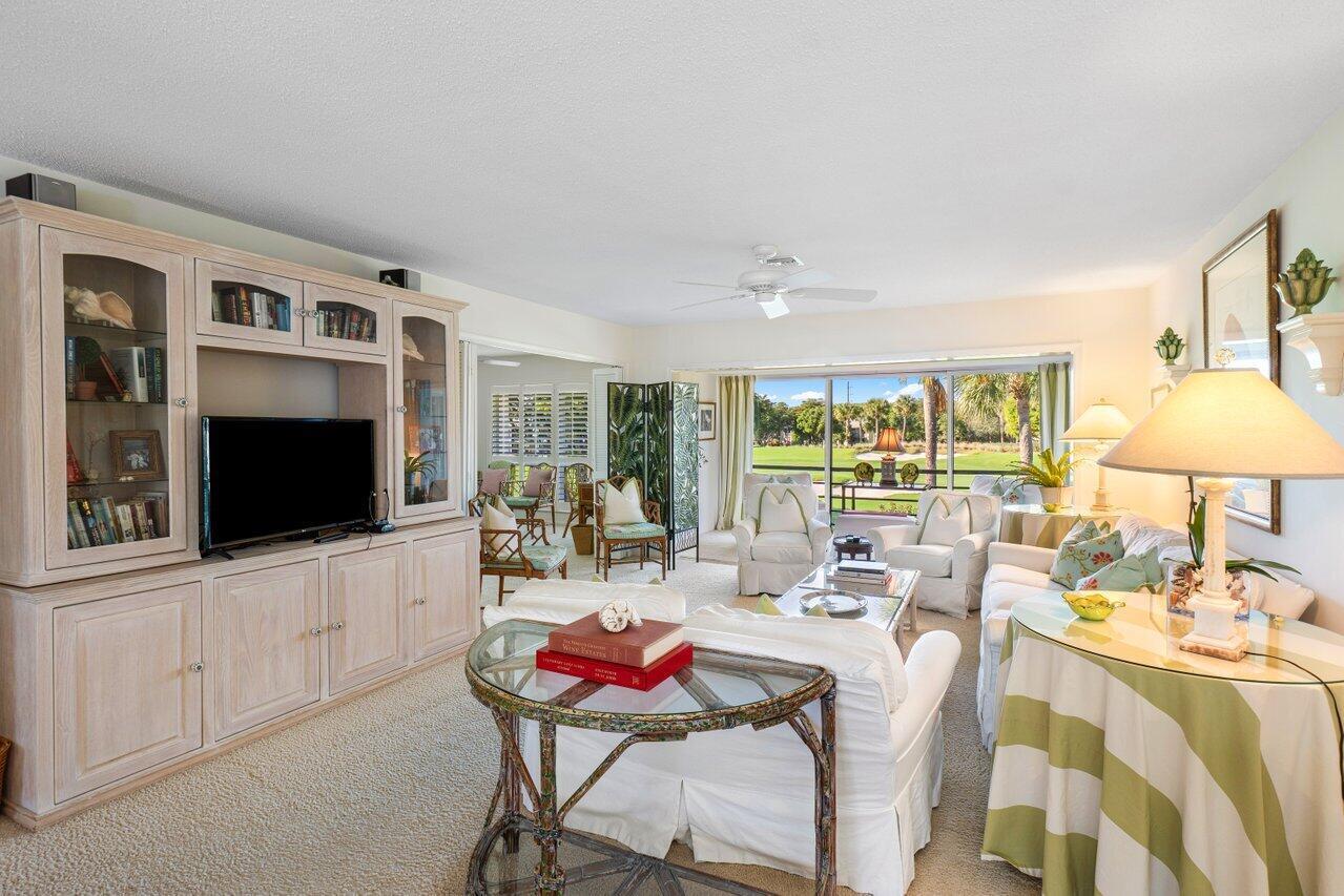 A living room features a large entertainment center, white furniture, and a view of greenery — 3870 Quail Ridge Drive, Boynton Beach FL 33436, BOYNTON BEACH, FL