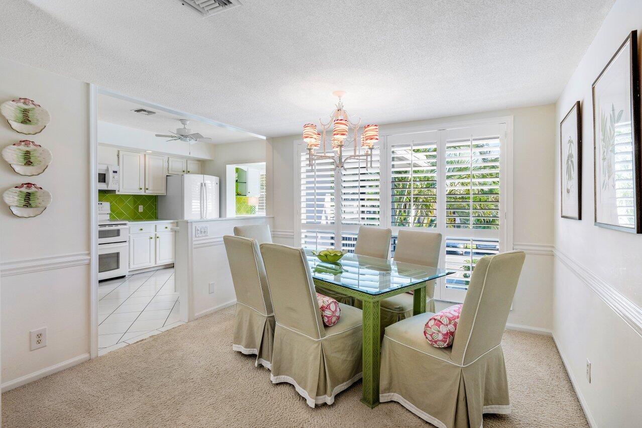 A dining room with a glass table, beige slipcovered chairs, and an adjacent white kitchen — 3870 Quail Ridge Drive, Boynton Beach FL 33436, BOYNTON BEACH, FL