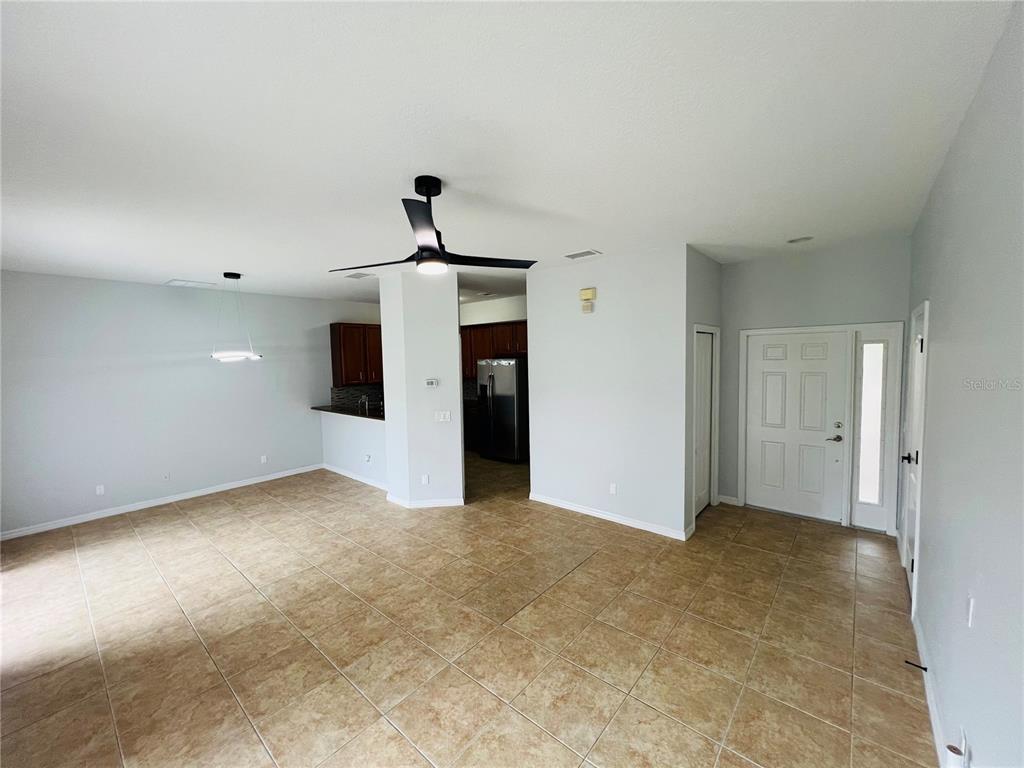 An open-concept living area features light-colored tile flooring, a ceiling fan, and a kitchen view — 9096 IRON OAK AVENUE, TAMPA, FL