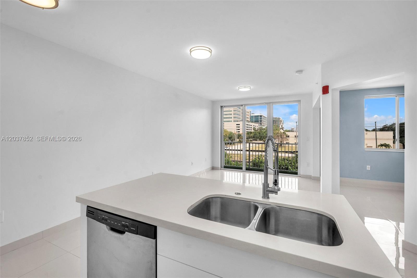 A kitchen island with a double sink and dishwasher overlooks an open living area — 2651 NE 212th Ter # 301, Miami FL 33180, MIAMI, FL