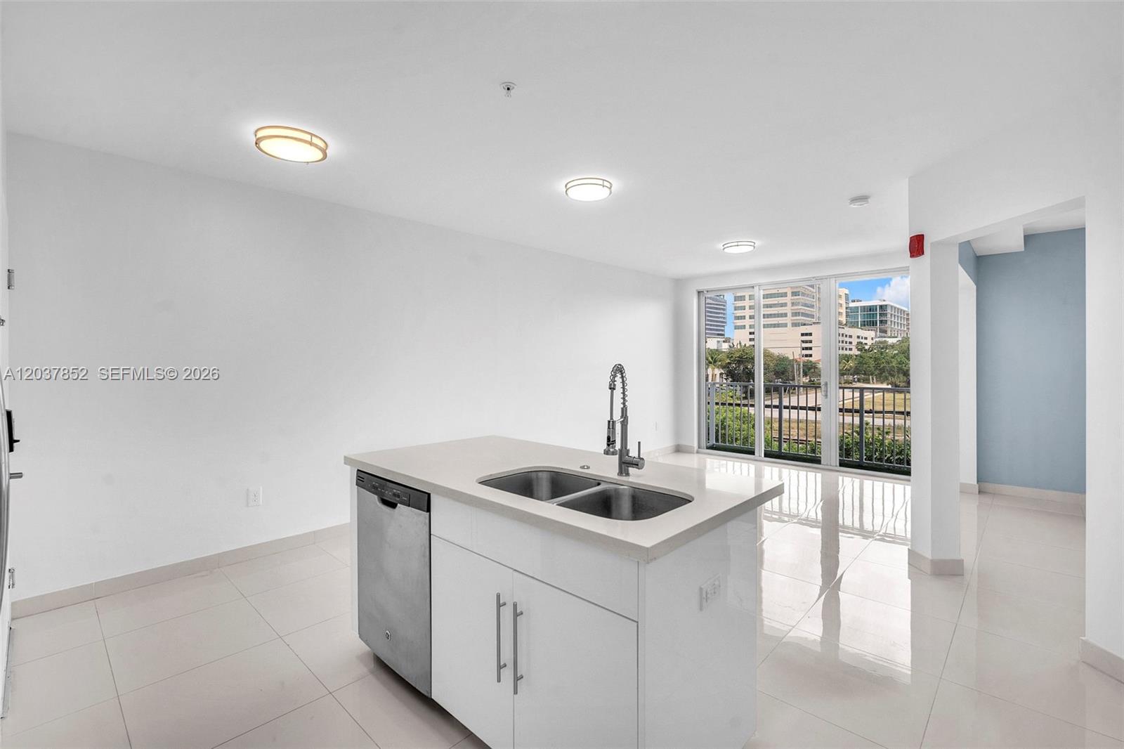 A kitchen island with a stainless steel dishwasher and sink sits in a white room — 2651 NE 212th Ter # 301, Miami FL 33180, MIAMI, FL