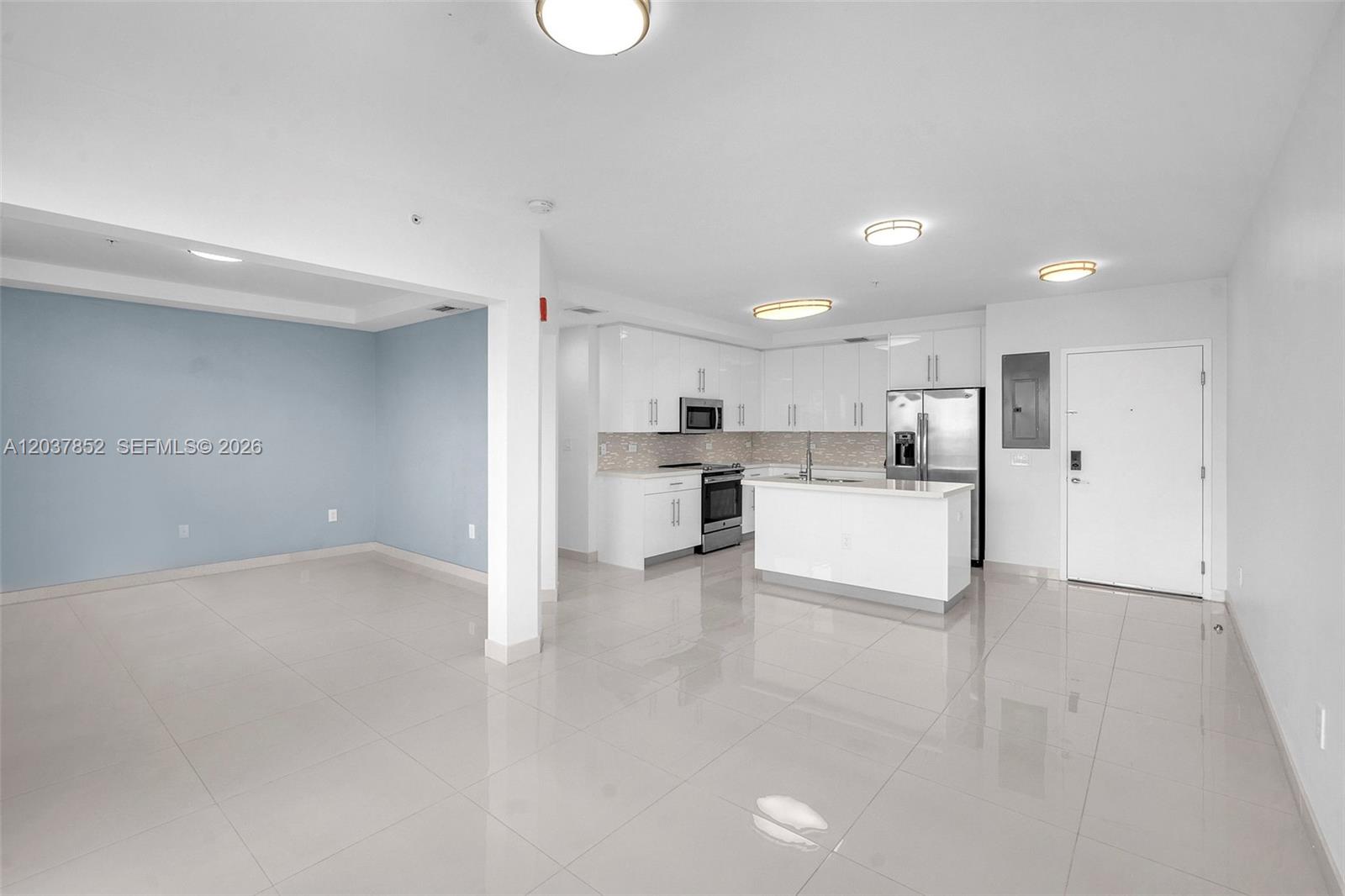 A kitchen with white cabinets and stainless steel appliances opens to a living area — 2651 NE 212th Ter # 301, Miami FL 33180, MIAMI, FL