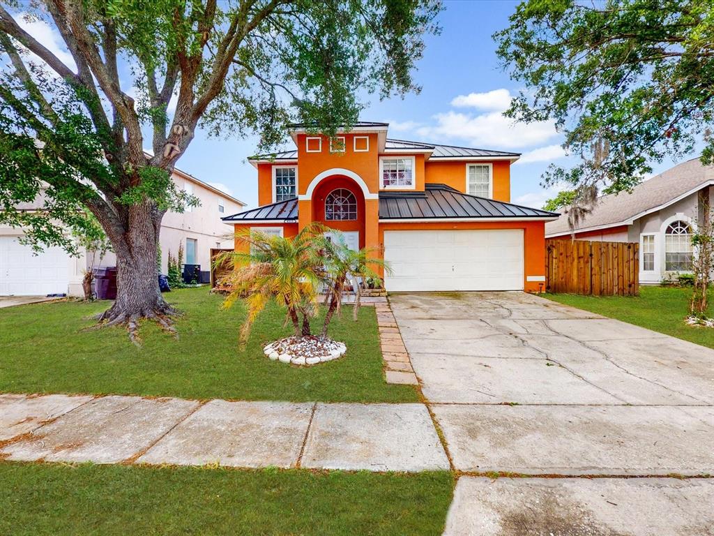 A two-story orange house with a metal roof and a concrete driveway sits on grass — 4313 BAY BROOK DRIVE, KISSIMMEE, FL