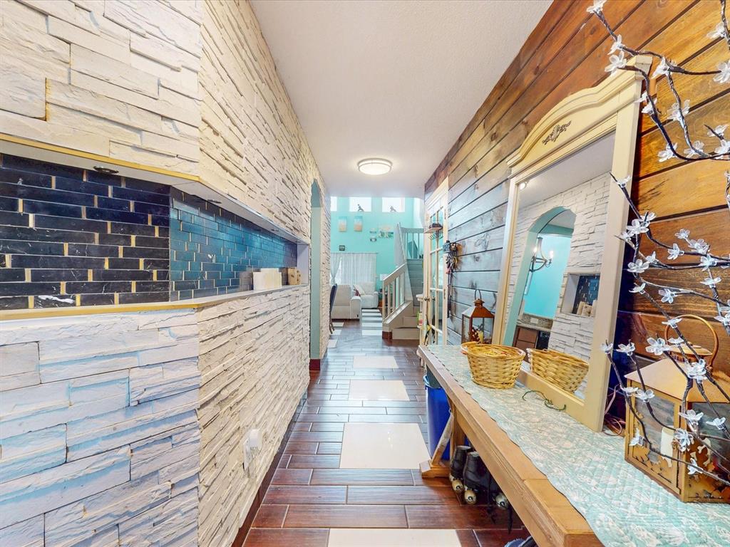 A hallway features a stone-accented wall, wood-paneled wall, and tile flooring leading toward stairs — 4313 BAY BROOK DRIVE, KISSIMMEE, FL