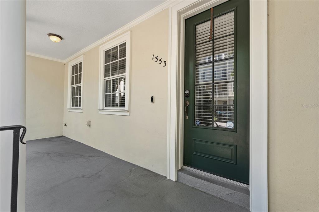 A covered porch features a dark green front door and two windows on a beige wall — 1353 CHATFIELD PLACE, ORLANDO, FL