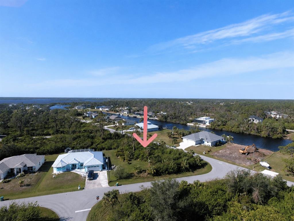 An aerial view shows a vacant, tree-covered lot situated between two houses near a canal — 13177 WINDCREST DRIVE, PORT CHARLOTTE, FL