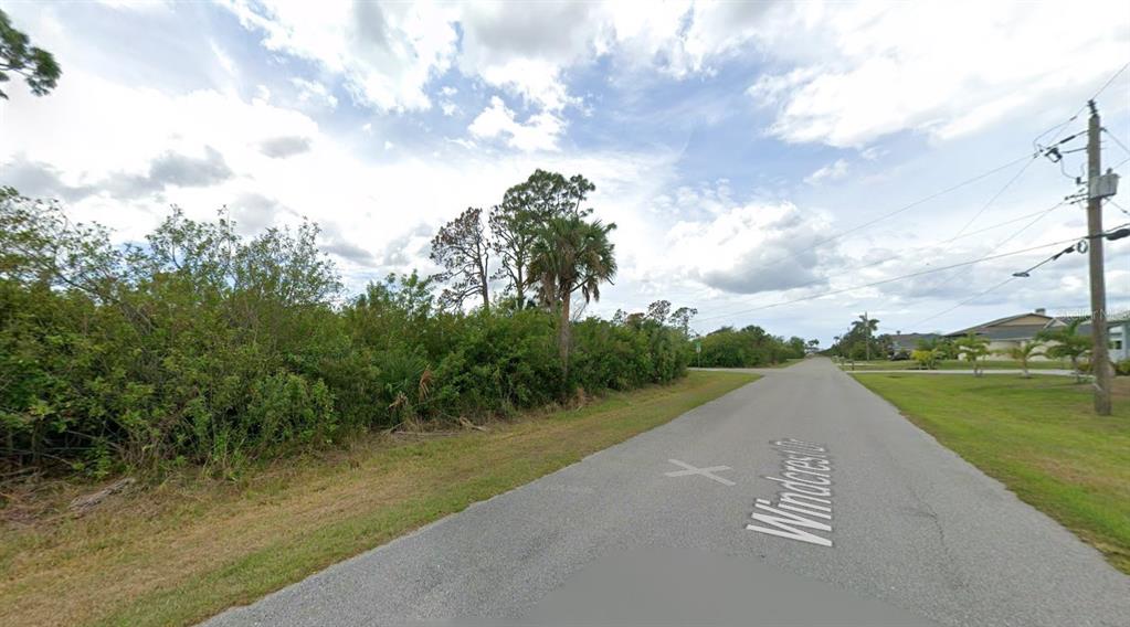 A paved road runs alongside a vacant, overgrown lot with trees and shrubs — 13177 WINDCREST DRIVE, PORT CHARLOTTE, FL