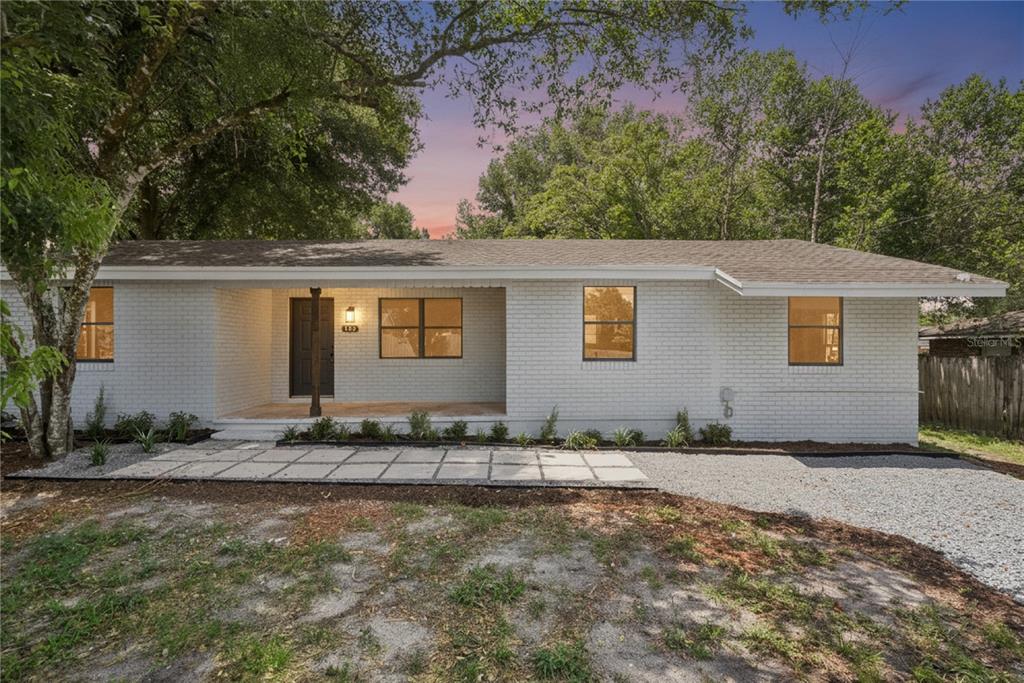 A single-story white brick house features a covered front porch and a paved walkway — 137 LUCERNE DRIVE, DEBARY, FL
