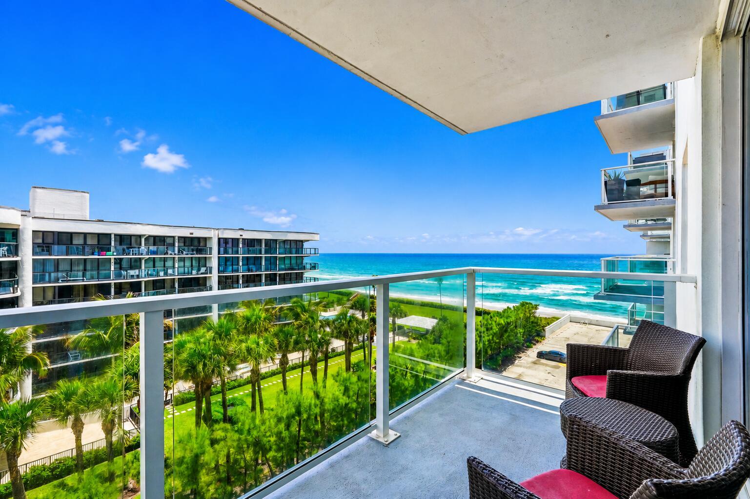 A balcony with wicker chairs overlooks a grassy courtyard, palm trees, and the ocean — 3450 S Ocean Boulevard # 6010, Palm Beach FL 33480, PALM BEACH, FL