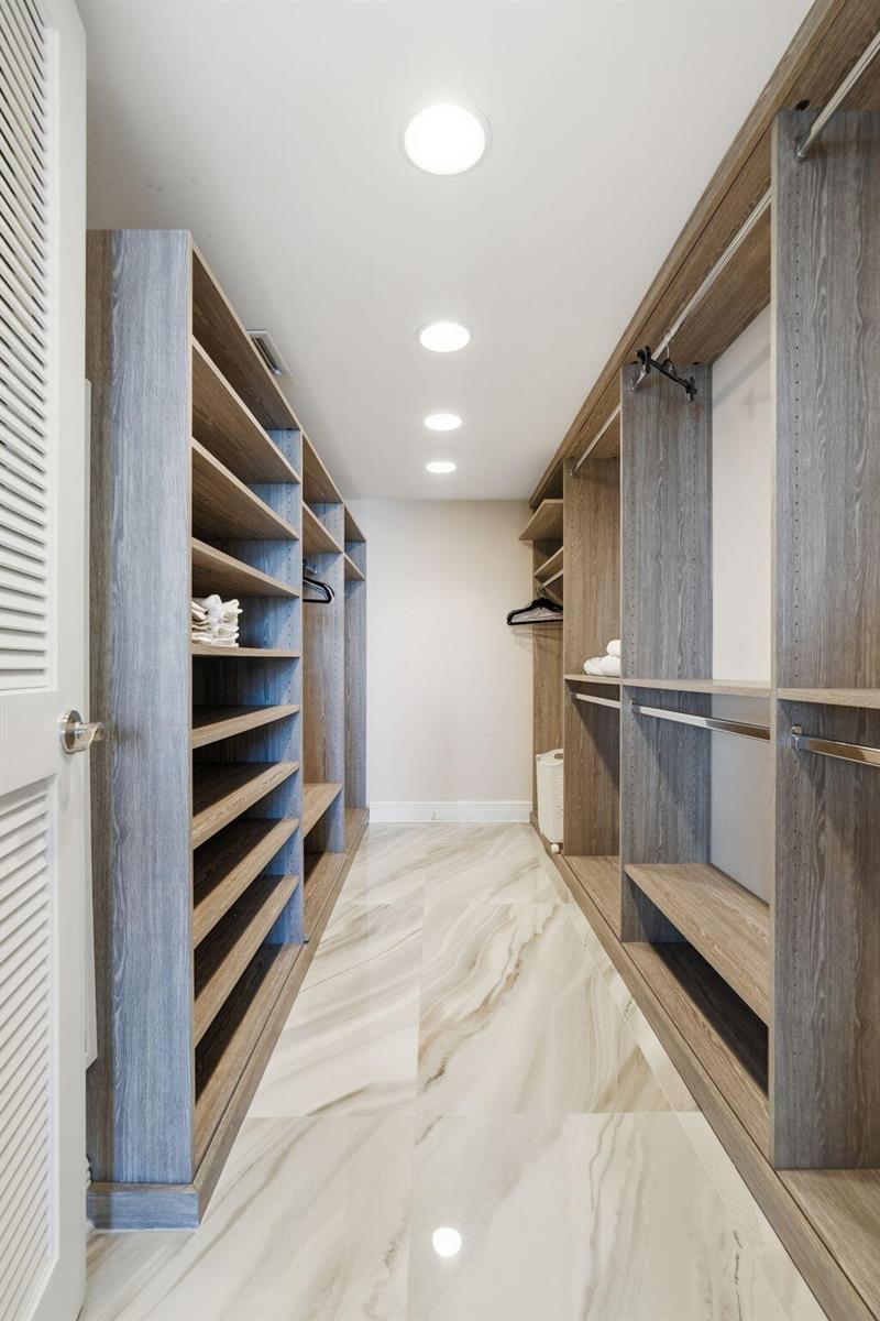 A walk-in closet features wood-grain shelving, hanging rods, and light-colored marble-look tile flooring — 3450 S Ocean Boulevard # 6010, Palm Beach FL 33480, PALM BEACH, FL