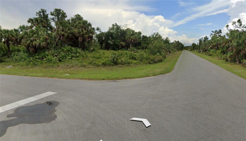 A paved road intersection is surrounded by dense green trees and vegetation under a cloudy sky — 14272 HOWARD AVENUE, PORT CHARLOTTE, FL