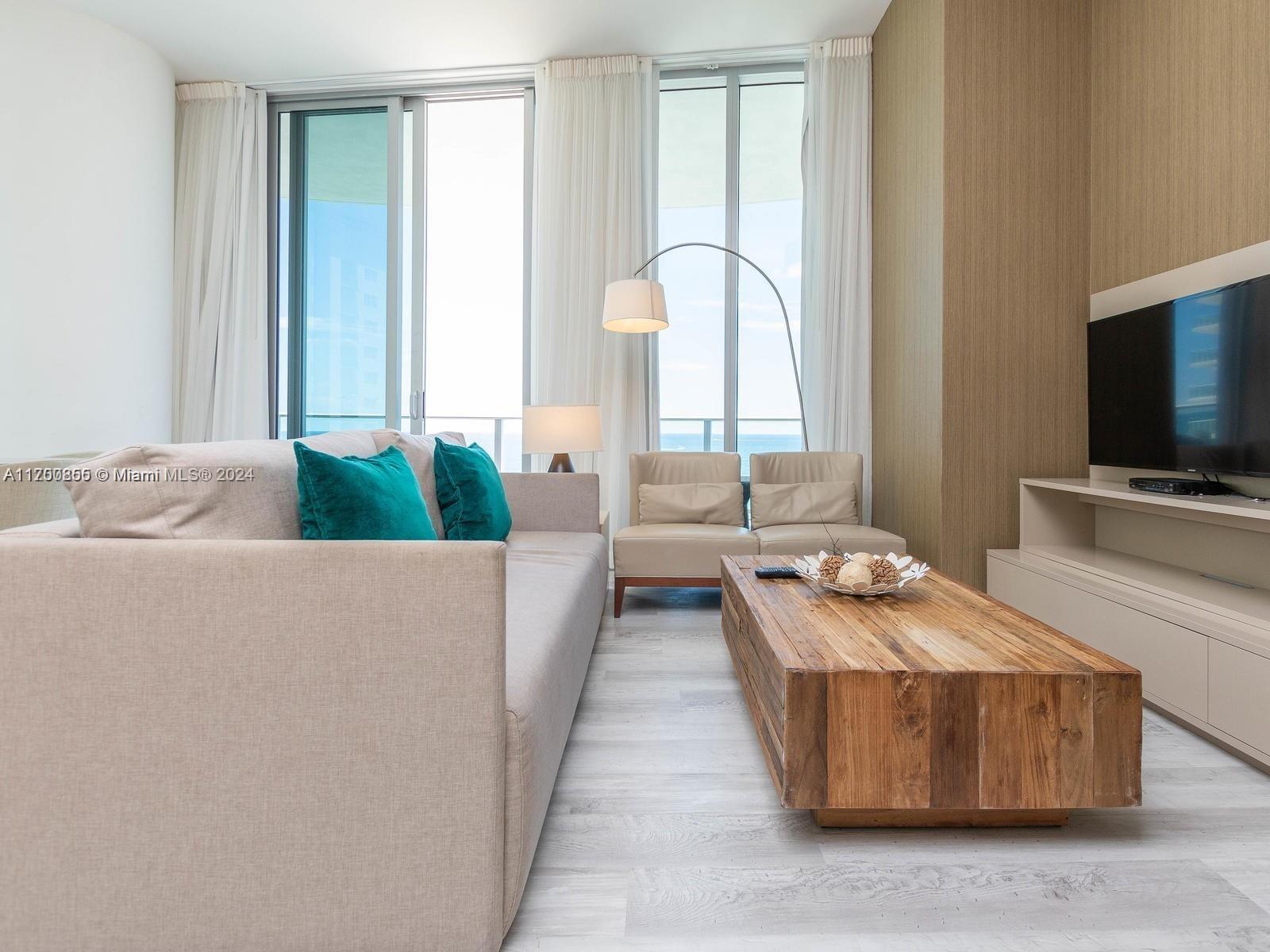 A living room features a beige sofa, wooden coffee table, and floor-to-ceiling windows with ocean views — 4111 S Ocean Dr # 601, Hollywood FL 33019, HOLLYWOOD, FL