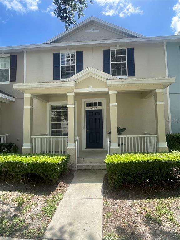 A two-story townhouse features a covered front porch, a dark blue door, and manicured hedges — 14392 BRIDGEWATER CROSSINGS BOULEVARD, WINDERMERE, FL