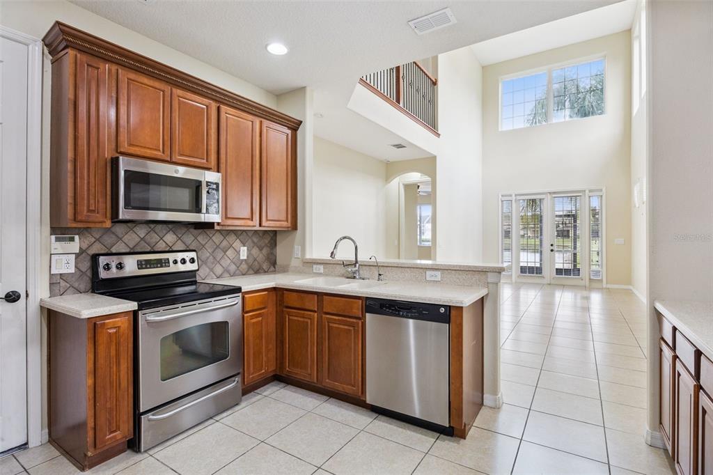 A kitchen with wood cabinets, stainless steel appliances, and tile flooring overlooks a living area — 551 TERRACE SPRING DRIVE, ORLANDO, FL