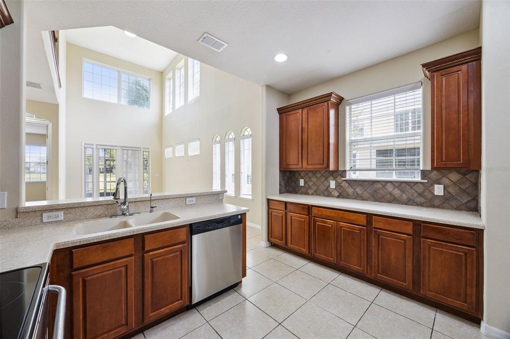 A kitchen with wood cabinets, tile flooring, and a view into a high-ceilinged living area — 551 TERRACE SPRING DRIVE, ORLANDO, FL