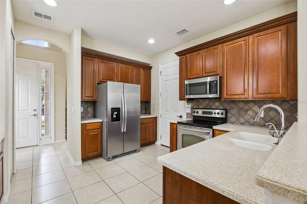 A kitchen with wood cabinets, stainless steel appliances, tile flooring, and a light-colored countertop — 551 TERRACE SPRING DRIVE, ORLANDO, FL