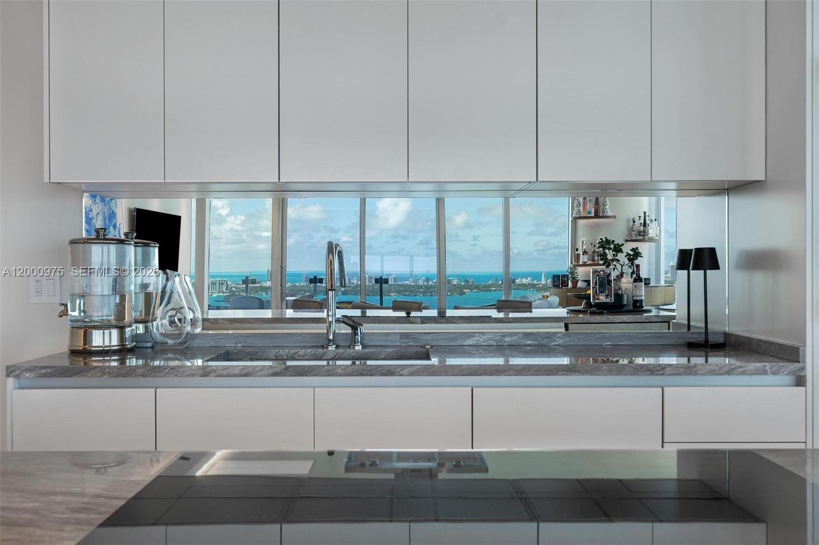 A modern kitchen features white cabinets, a marble countertop, and a mirrored backsplash with views — 700 NE 26th Ter # 3901, Miami FL 33137, MIAMI, FL