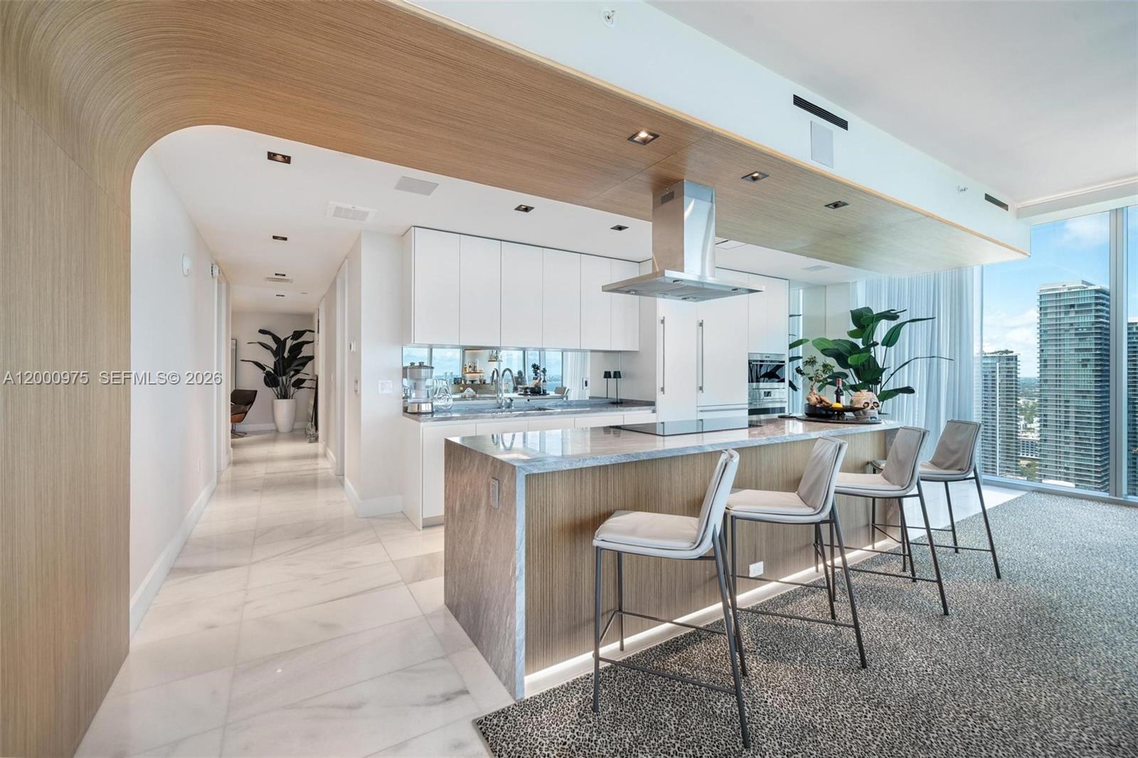A modern kitchen features a marble-topped island, wood paneling, and floor-to-ceiling windows with city views — 700 NE 26th Ter # 3901, Miami FL 33137, MIAMI, FL