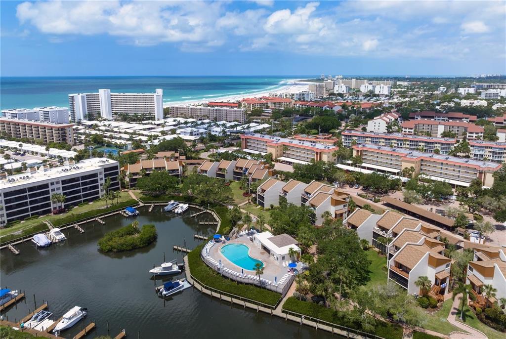 An aerial view shows a waterfront condominium complex with a pool, boat slips, and beach — 1400 COVE II PLACE UNIT 631, SARASOTA, FL