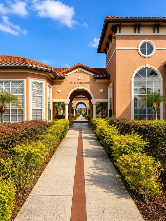 A paved walkway leads through a Mediterranean-style clubhouse entrance with arched doorways and landscaping — 5542 METROWEST BOULEVARD UNIT 7-104, ORLANDO, FL