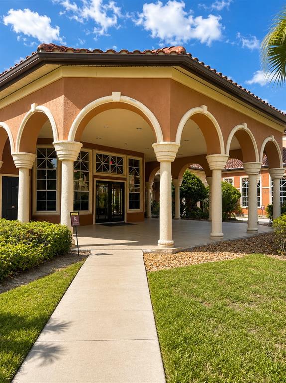 A concrete walkway leads to the arched, covered entrance of a tan stucco building — 5542 METROWEST BOULEVARD UNIT 7-104, ORLANDO, FL