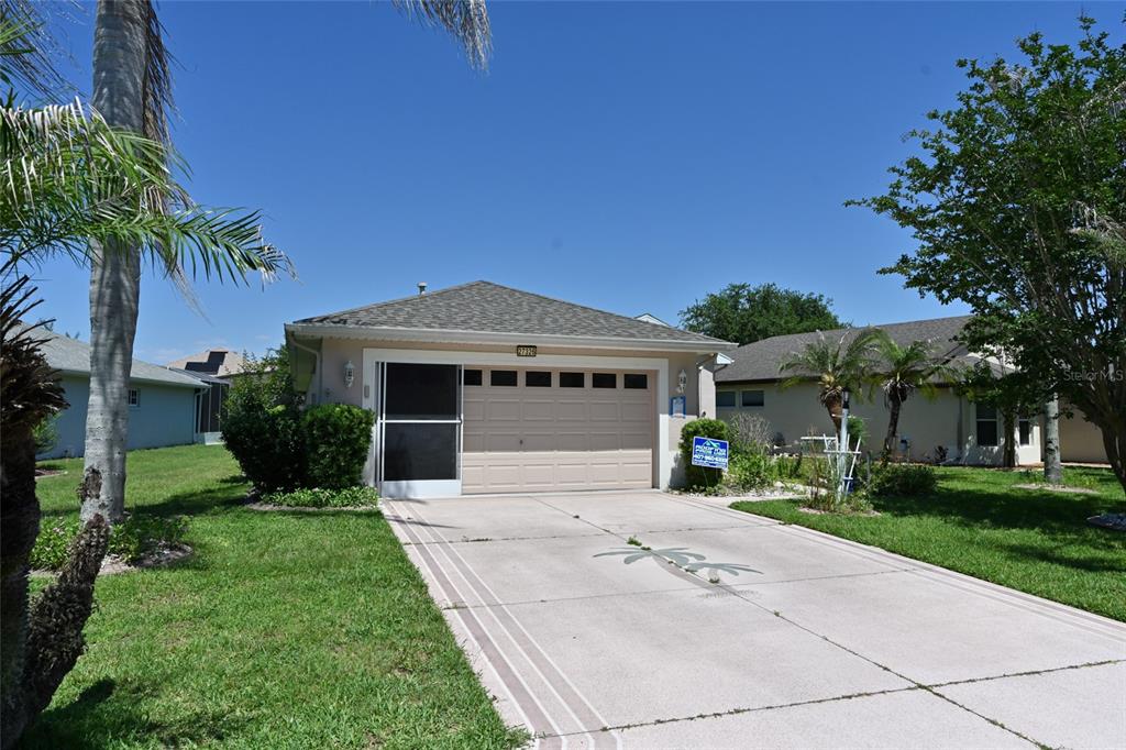 A single-story house with a beige garage door, a screened entryway, and a concrete driveway — 27326 ORCHID GLADE STREET, LEESBURG, FL