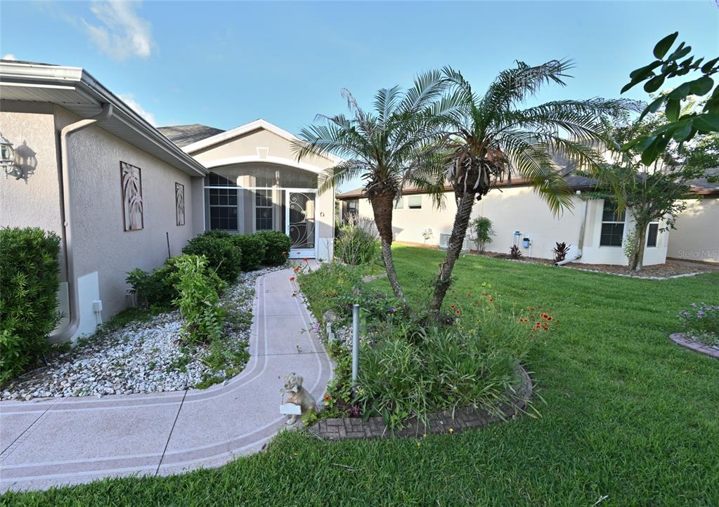 A concrete walkway leads to the screened front entrance of a house with palm trees — 27326 ORCHID GLADE STREET, LEESBURG, FL