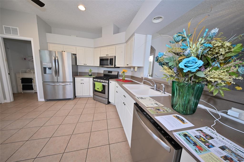 A kitchen features white cabinets, stainless steel appliances, tile flooring, and a large floral centerpiece — 27326 ORCHID GLADE STREET, LEESBURG, FL