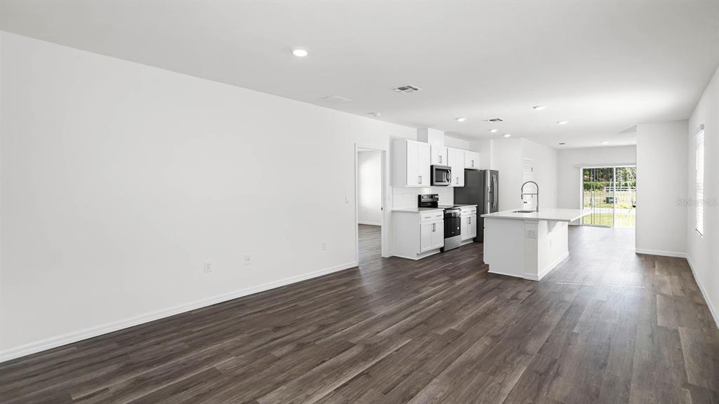 An open-concept kitchen and living area features white cabinetry, a center island, and wood-look flooring — 1628 HUMMINGBIRD ROAD, WINTER HAVEN, FL