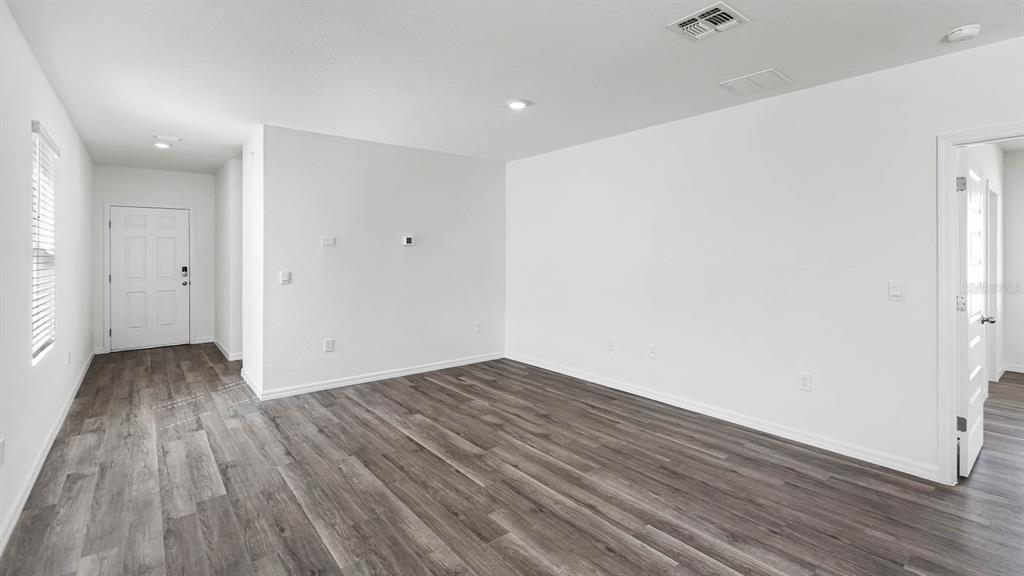 An empty room with white walls and gray wood-look flooring features a white door — 1628 HUMMINGBIRD ROAD, WINTER HAVEN, FL