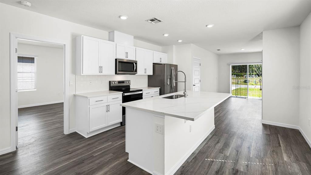 A modern kitchen features white cabinets, a large island with a sink, and gray flooring — 1628 HUMMINGBIRD ROAD, WINTER HAVEN, FL