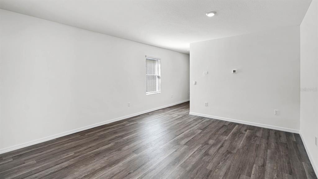 An empty room features white walls, dark wood-look flooring, and a single window — 1628 HUMMINGBIRD ROAD, WINTER HAVEN, FL